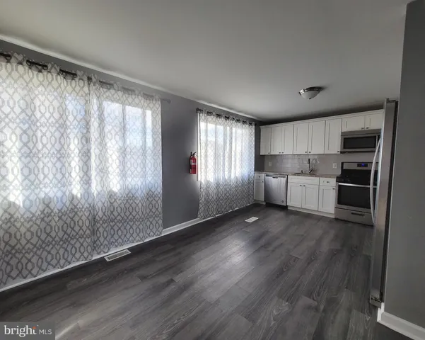 a kitchen with stainless steel appliances granite countertop a refrigerator a sink dishwasher a stove and white countertops with wooden floor