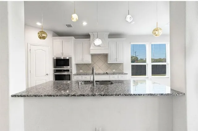 a kitchen with kitchen island granite countertop a stove a sink and a granite counter tops with white cabinets