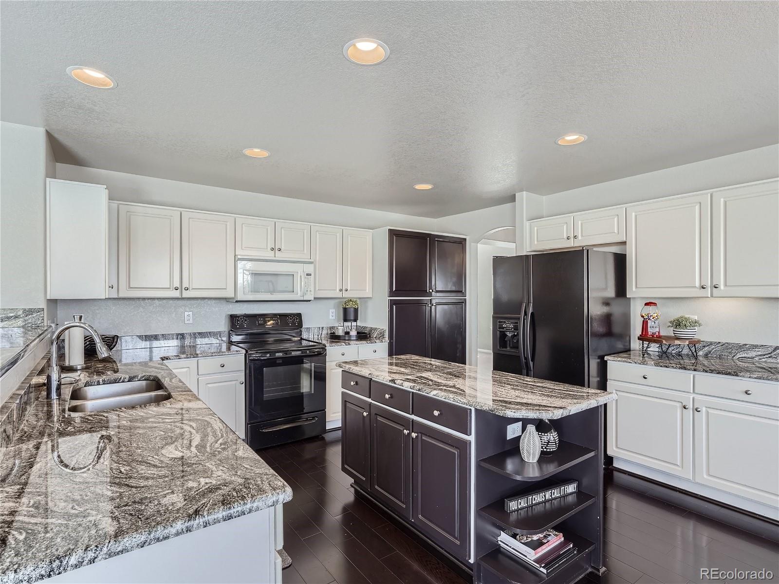 6596 Millstone Street Highlands Ranch, CO 80130 - Photo 9 of 33 a kitchen with kitchen island granite countertop stainless steel appliances a stove refrigerator sink and microwave