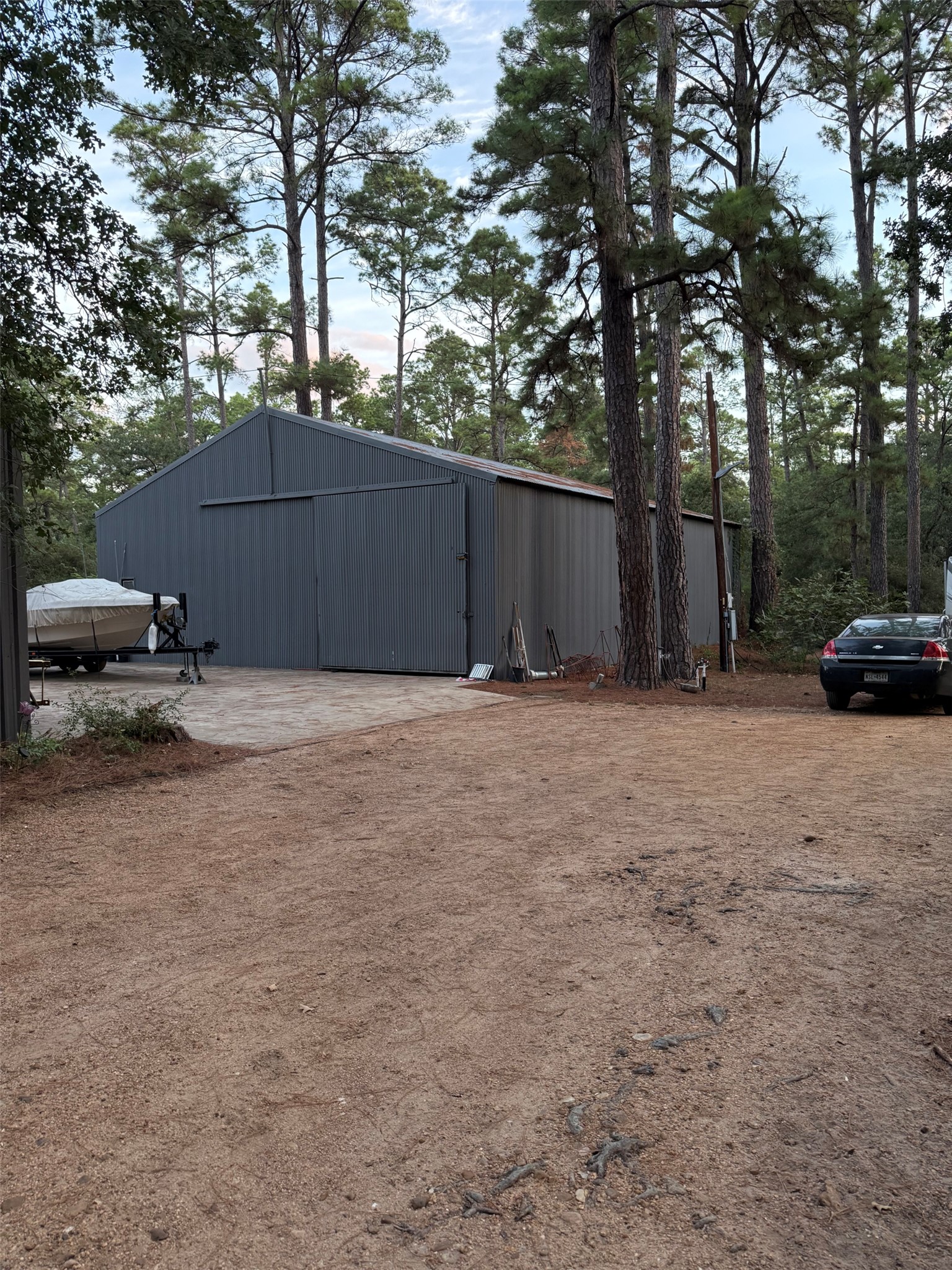 363 Porter Road Bastrop, TX 78602 - Photo 5 of 37 Mature trees frame a substantial metal outbuilding with sliding doors and a spacious dirt driveway.