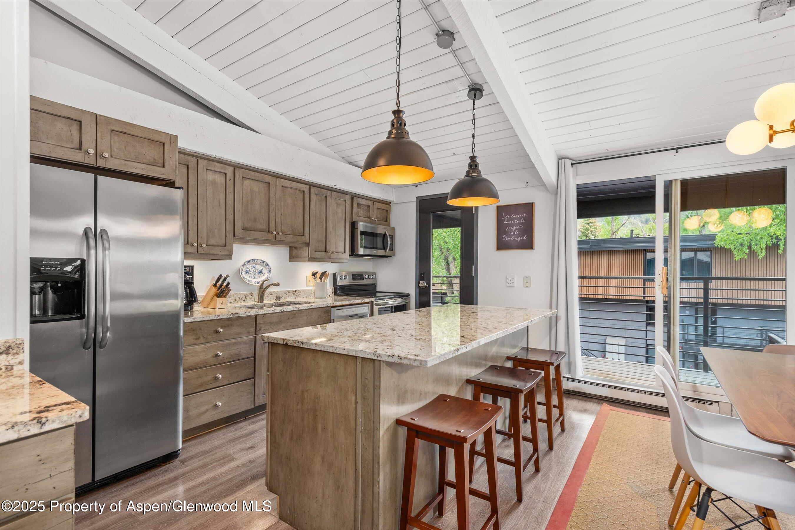 1039 East Cooper Avenue, Unit 36B Aspen, CO 81611 - Photo 7 of 15 a kitchen with stainless steel appliances granite countertop a stove a refrigerator a sink dishwasher a dining table and chairs with wooden floor