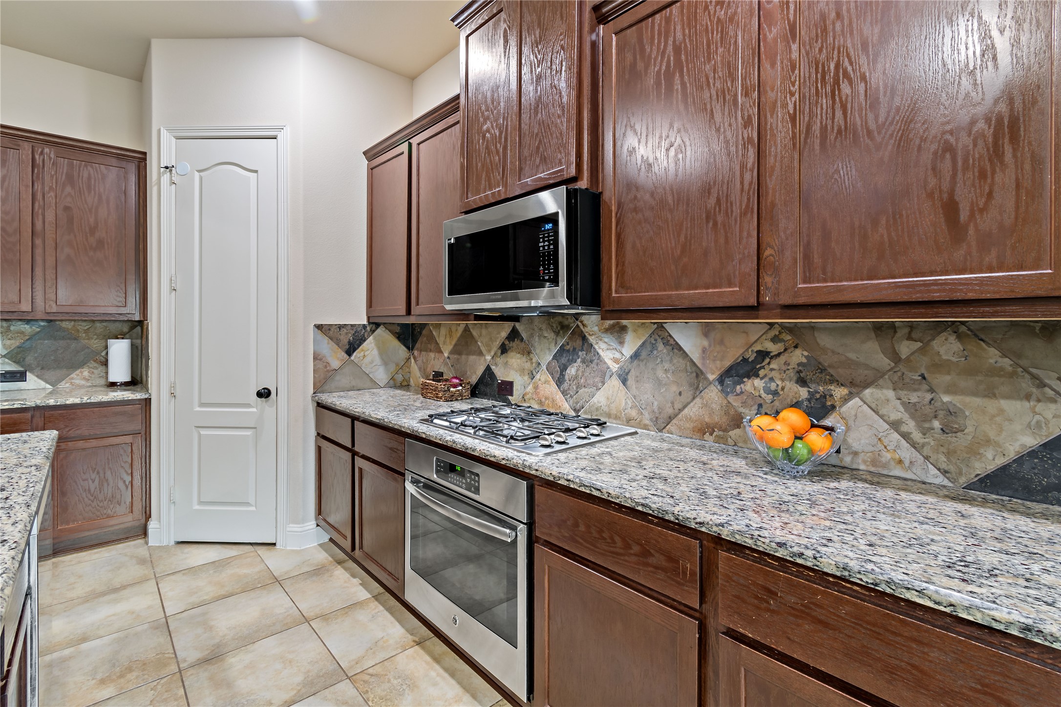 8126 Spreadwing Street Conroe, TX 77385 - Photo 14 of 30 Modern kitchen with stainless steel appliances, granite countertops, and rich wooden cabinetry. Features a slate backsplash and ample storage space. Walk in pantry