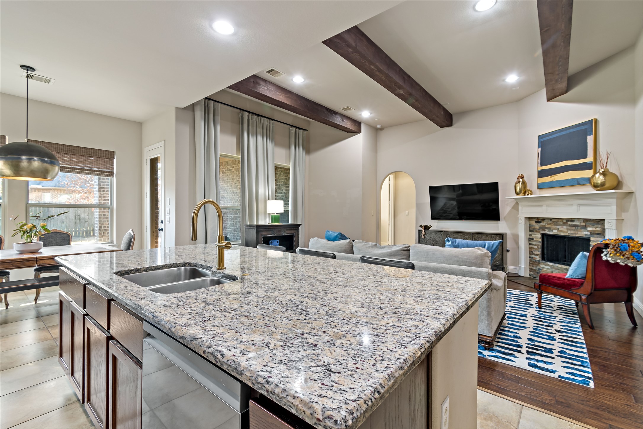 8126 Spreadwing Street Conroe, TX 77385 - Photo 17 of 30 This open-concept living area features a modern kitchen island with granite countertops, a cozy living room with a gas fireplace, and exposed wooden beams. Large windows and stylish decor create a bright and inviting space, perfect for entertaining or relaxing.