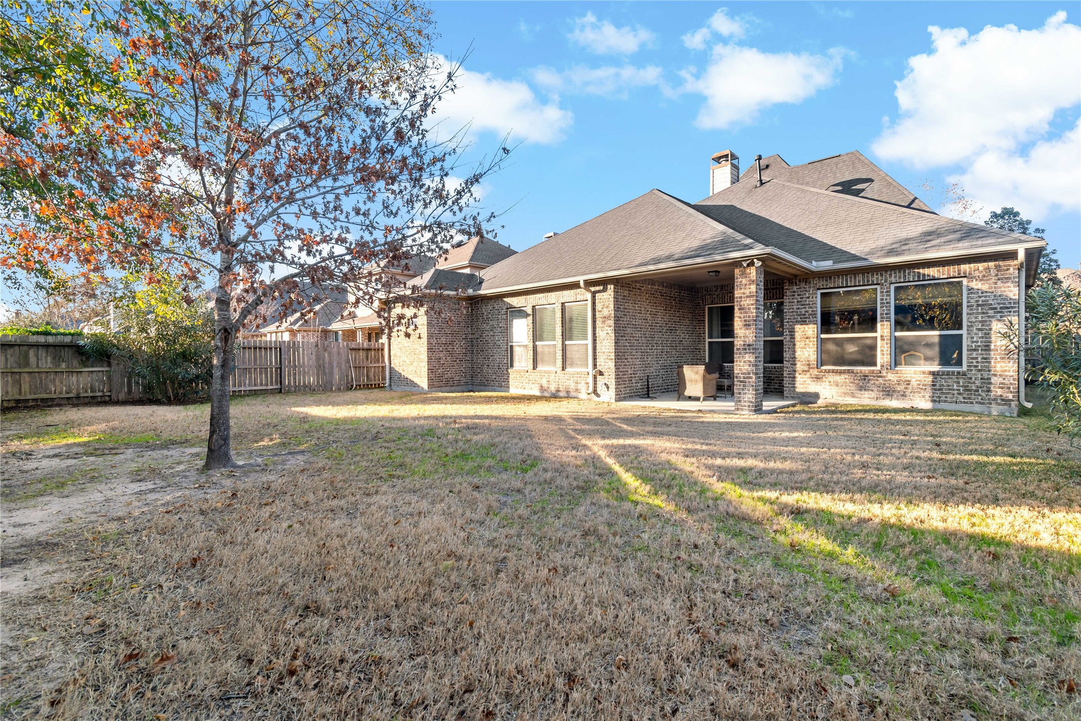8126 Spreadwing Street Conroe, TX 77385 - Photo 2 of 30 This photo shows a spacious backyard with a single-story brick house. The yard features a tree and a grassy area, providing ample outdoor space. The house has large windows and a covered patio area, perfect for outdoor activities and relaxation.