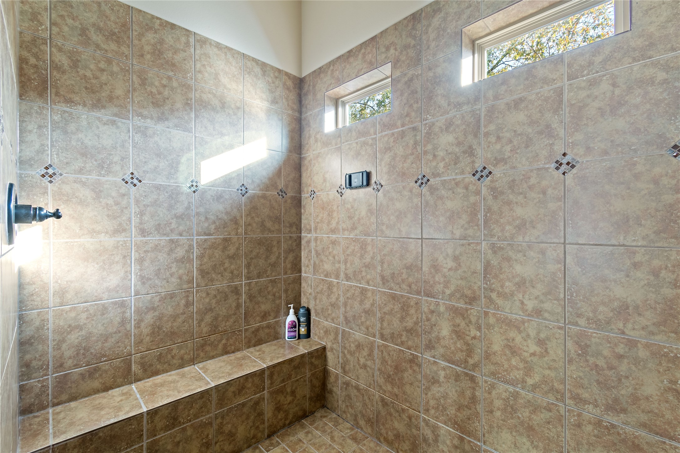 8126 Spreadwing Street Conroe, TX 77385 - Photo 23 of 30 This primary bathroom shows a spacious walk-in shower with tiled walls and a built-in bench. Natural light streams in through small windows, creating a bright and inviting atmosphere.
