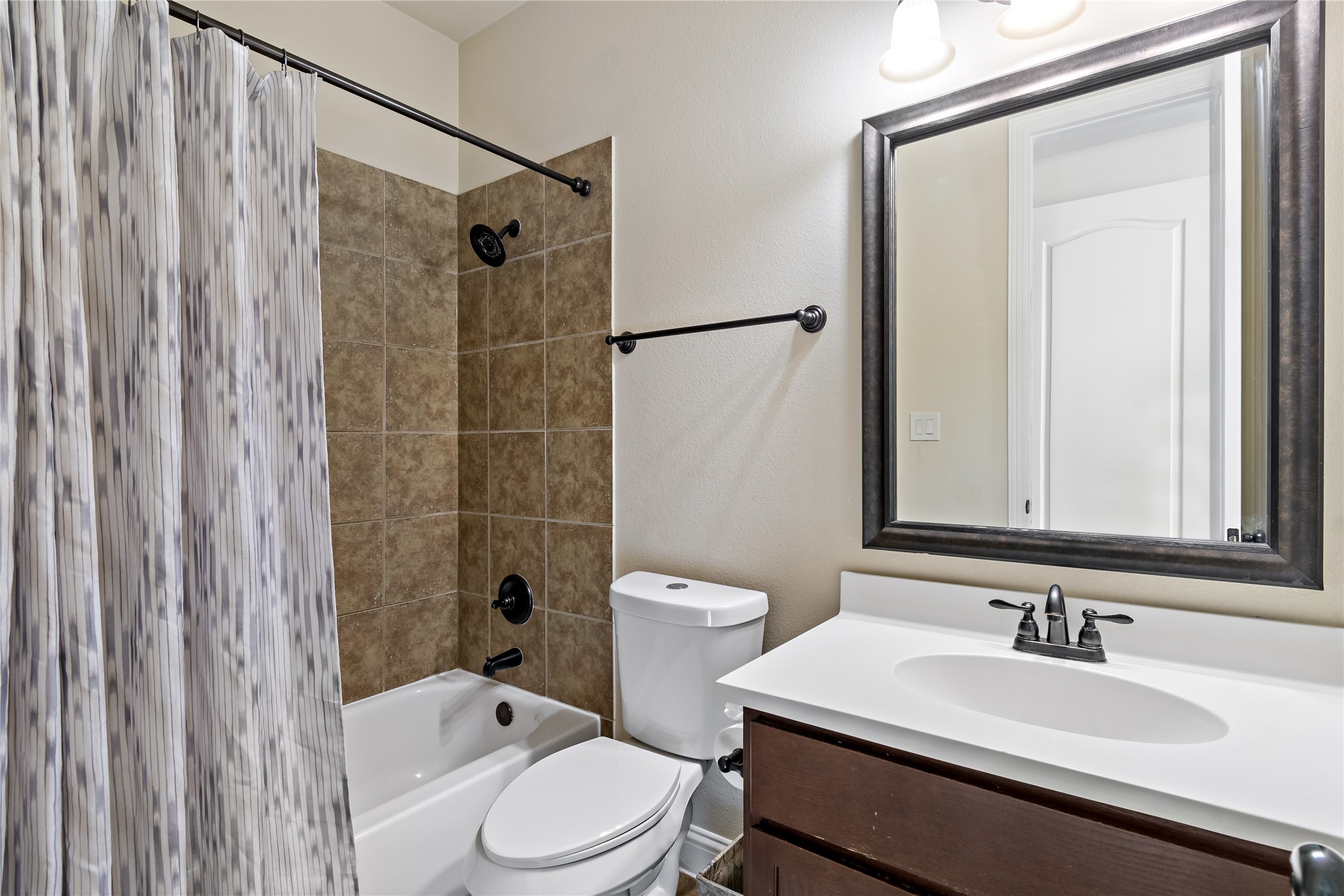 8126 Spreadwing Street Conroe, TX 77385 - Photo 26 of 30 This secondary bathroom features a shower-tub combo with a patterned curtain, a modern vanity with a dark wood finish, and a large mirror. The space is well-lit with overhead lighting and offers a clean, neutral design.