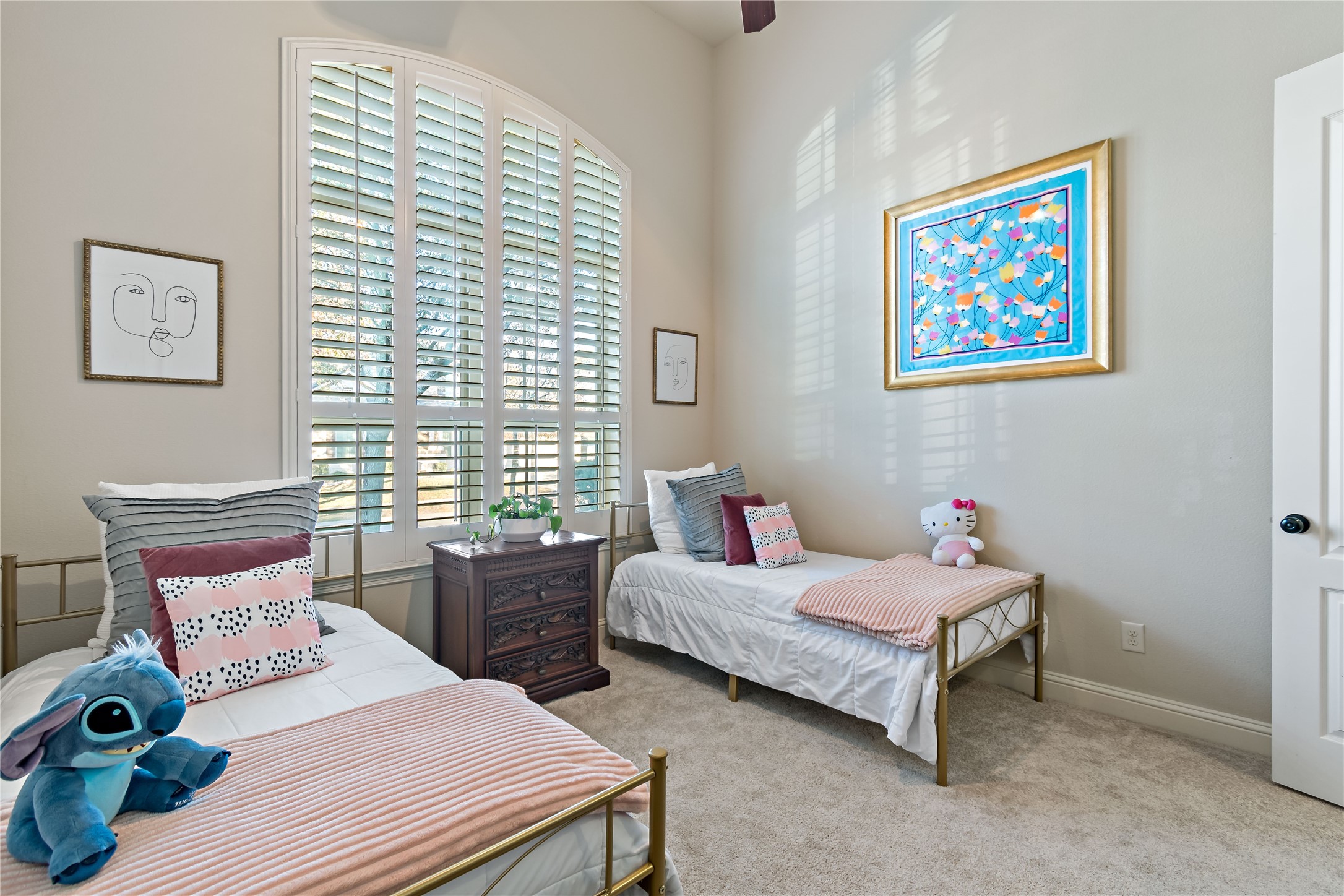 8126 Spreadwing Street Conroe, TX 77385 - Photo 27 of 30 Cozy bedroom with neutral tones features two twin beds, plush carpeting, and a large window with plantation shutters for natural light. Decor includes colorful wall art and playful accents, creating a welcoming space.