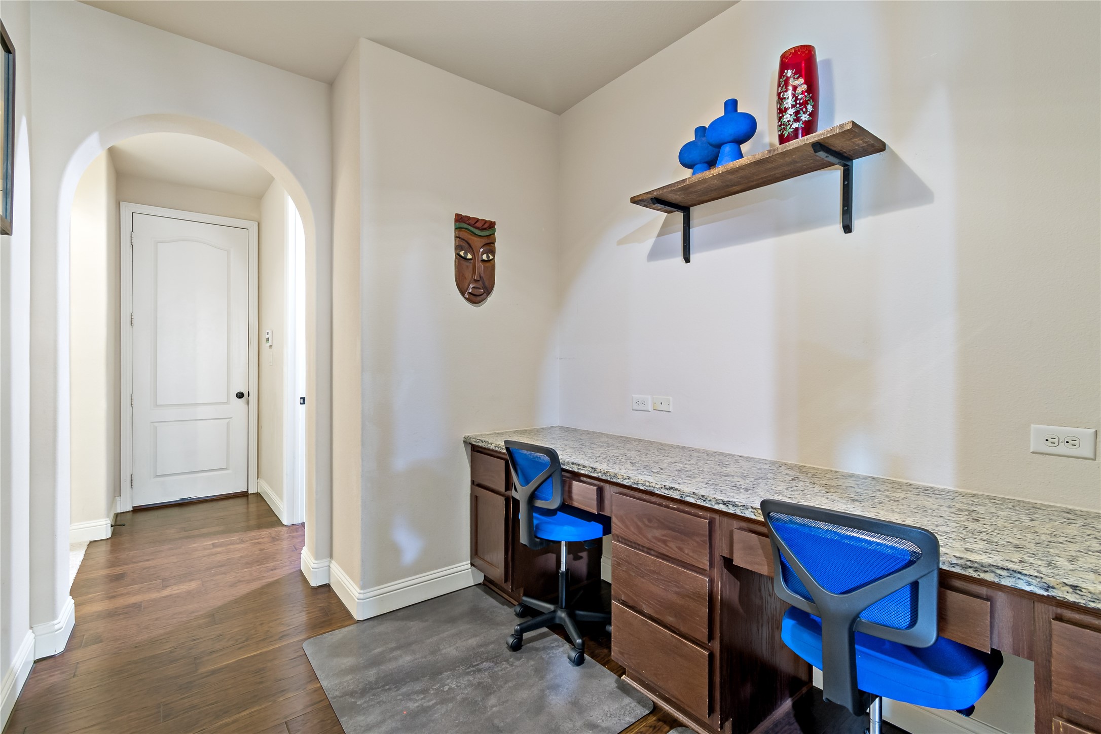 8126 Spreadwing Street Conroe, TX 77385 - Photo 9 of 30 This photo shows a hallway with a built-in desk featuring granite countertops. There's a shelf above with decorative items, hardwood flooring, and an arched doorway leading to another room. Built in for homework