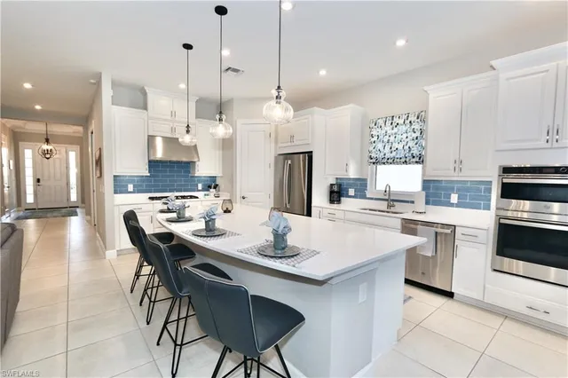 a kitchen with stainless steel appliances kitchen island granite countertop a dining table chairs and white cabinets