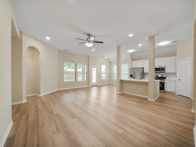 a view of an empty room with kitchen and window