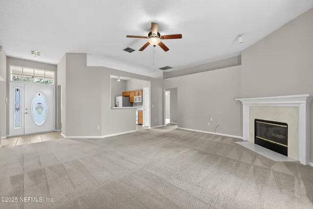 a view of an empty room with chandelier fan and fire place