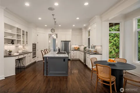a kitchen with stainless steel appliances kitchen island granite countertop a table chairs stove and white cabinets