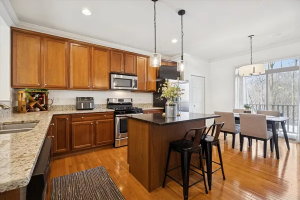 a kitchen with stainless steel appliances granite countertop a stove top oven a sink a dining table and chairs with wooden floor