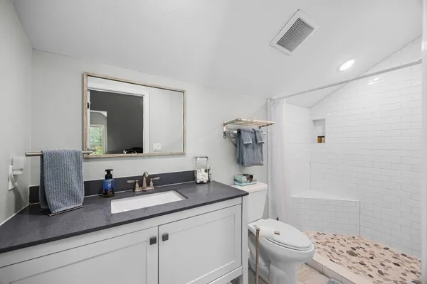 a bathroom with a granite countertop sink a toilet a mirror and shower