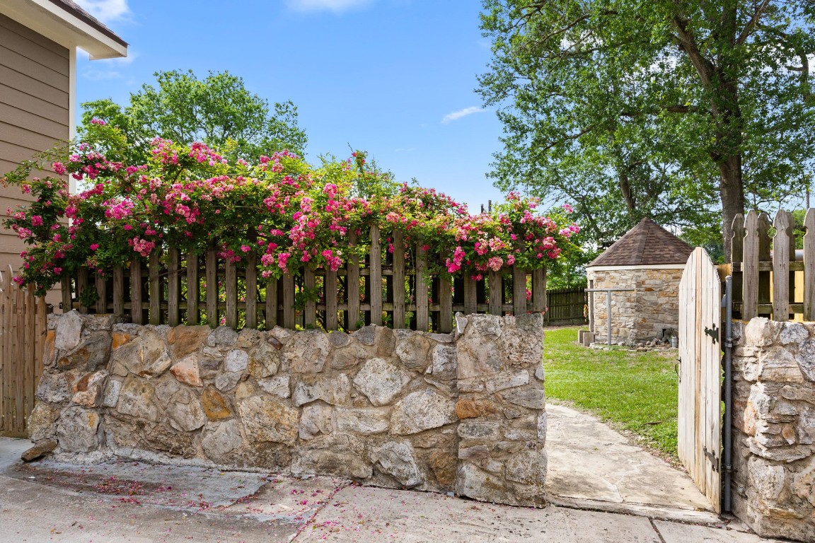 801 West Main Street Brenham, TX 77833 - Photo 43 of 50 A charming stone wall and gated entry welcome you into the backyard, accented by mature landscaping and blooming climbing roses that create a private and picturesque setting.