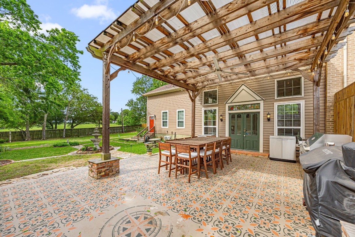 801 West Main Street Brenham, TX 77833 - Photo 44 of 50 The backyard is designed for entertaining with an expansive covered pergola featuring decorative concrete, a ceiling fan, and ample room for outdoor dining and gatherings, all overlooking the beautifully landscaped yard.