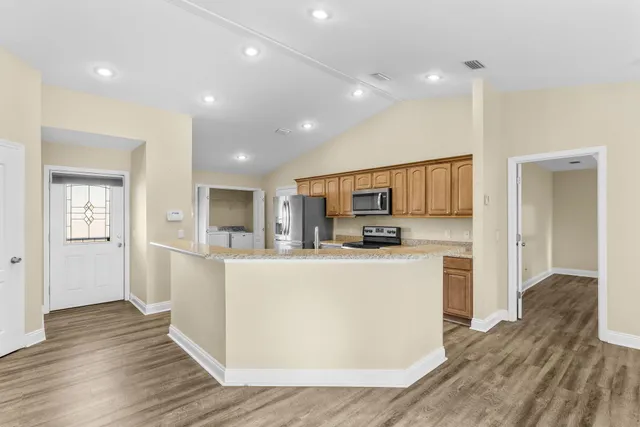 a living room with stainless steel appliances kitchen island wooden floors and kitchen view