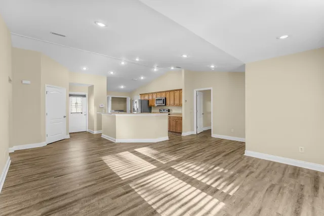 a view of an empty room with wooden floor and a kitchen