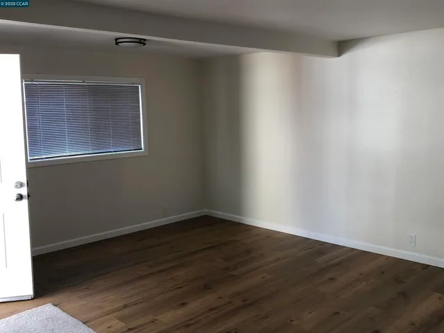 a view of an empty room with wooden floor and a window