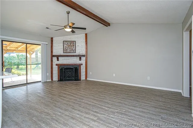 a view of an empty room with wooden floor fireplace and a window