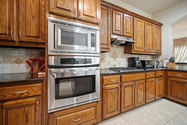 a kitchen with stainless steel appliances granite countertop a stove top oven a sink dishwasher a dining table and chairs with wooden floor