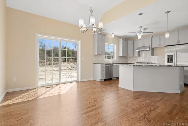 a open kitchen with granite countertop a stove top oven a sink dishwasher and white cabinets with wooden floor
