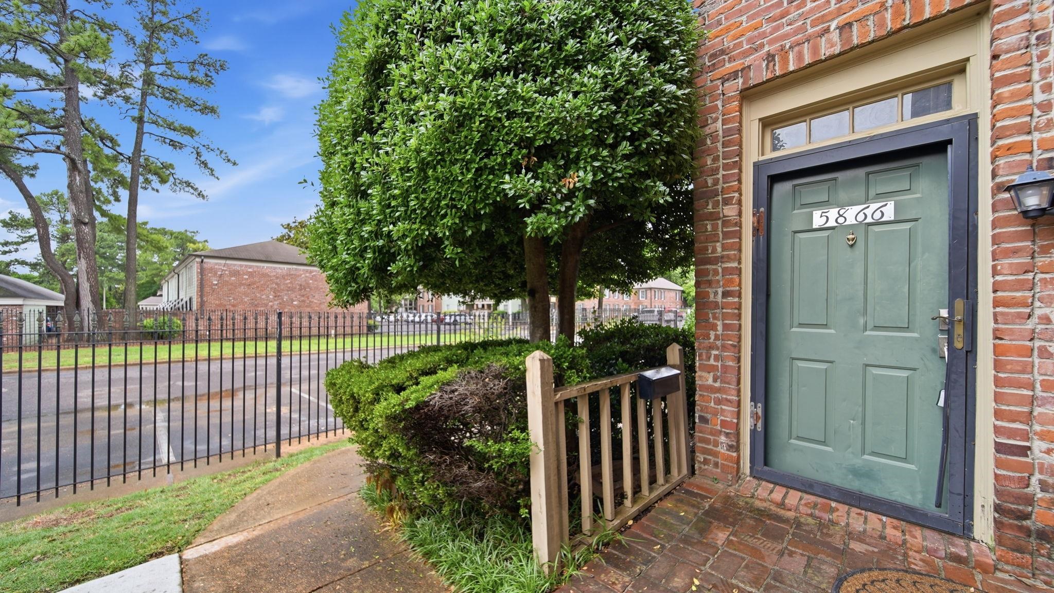 5866 Roxbury Drive, Unit 5866 Memphis, TN 38119 - Photo 1 of 20 Brick exterior featuring a paneled green entry door with transom window, exterior lighting, and a wrought iron fence