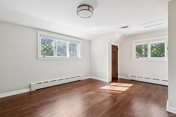 an empty room with wooden floor mirror and windows