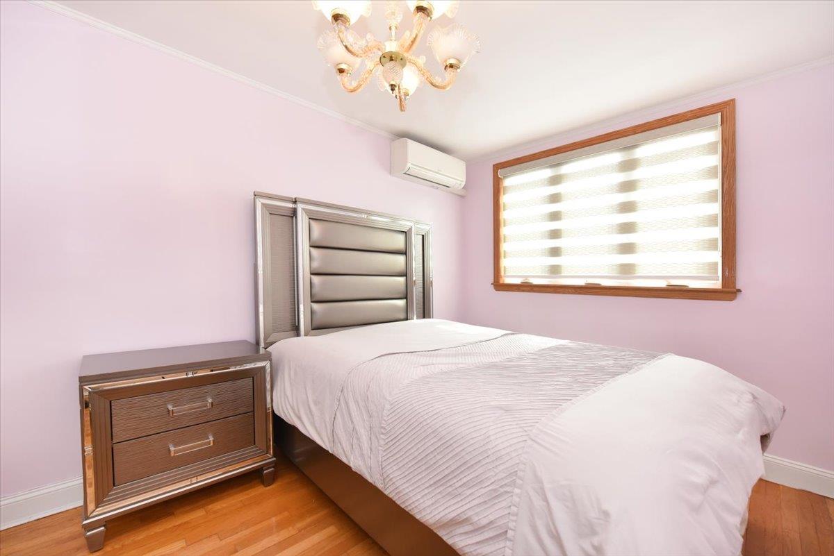 150-15 78th Road Queens, NY 11367 - Photo 18 of 28 Bedroom with an AC wall unit, a notable chandelier, light wood-style floors, and baseboards