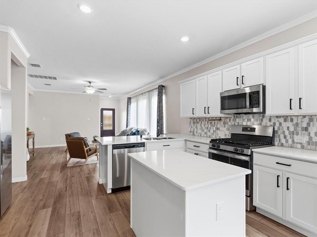 16936 Post Cedar Drive Justin, TX 76247 - Photo 8 of 30 Modern kitchen featuring white shaker cabinetry, stainless steel appliances, a center island with a solid surface countertop, and wood-finish flooring