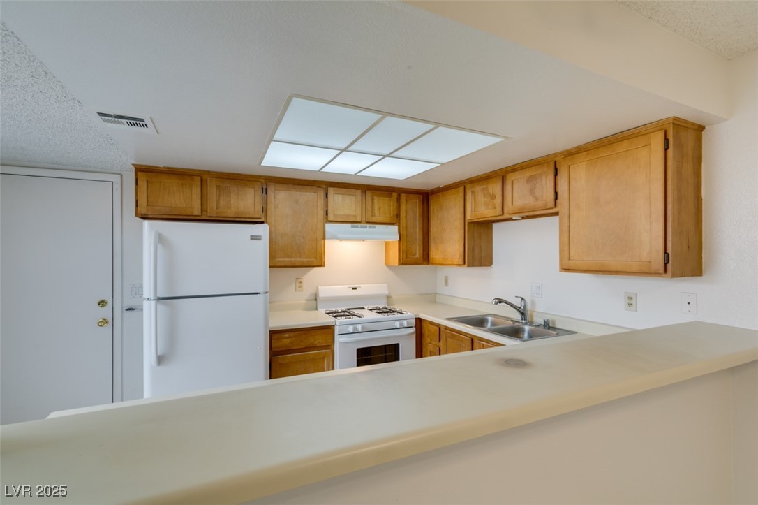 2681 Ruthe Duarte Avenue Las Vegas, NV 89121 - Photo 23 of 43 Kitchen featuring white appliances, light countertops, under cabinet range hood, visible vents, and a sink