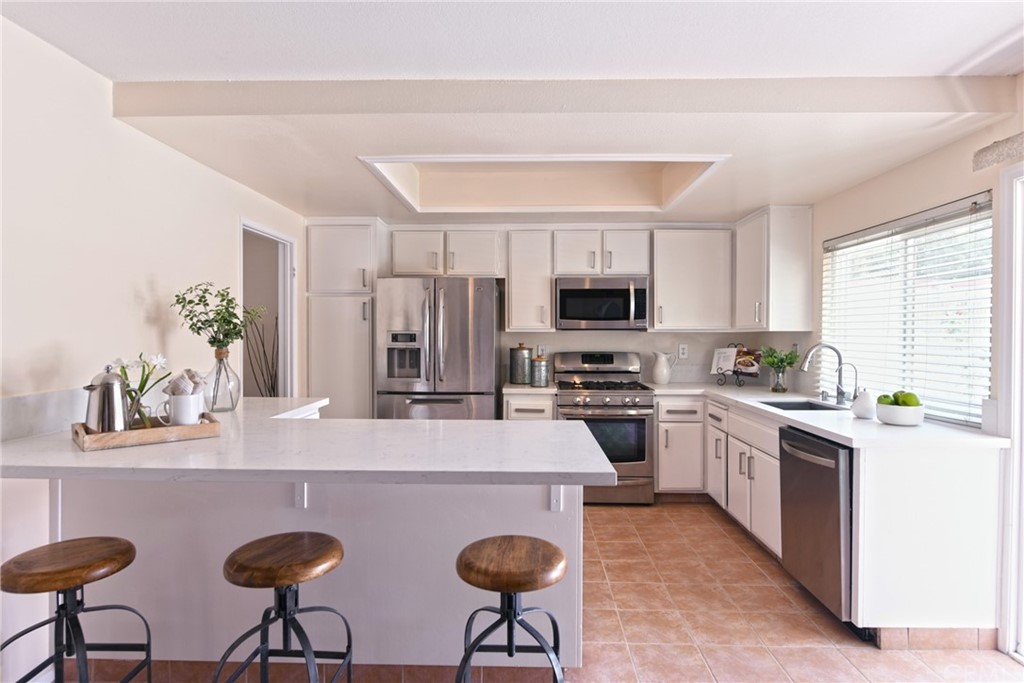 a kitchen with stainless steel appliances a sink a stove a refrigerator cabinets and chairs