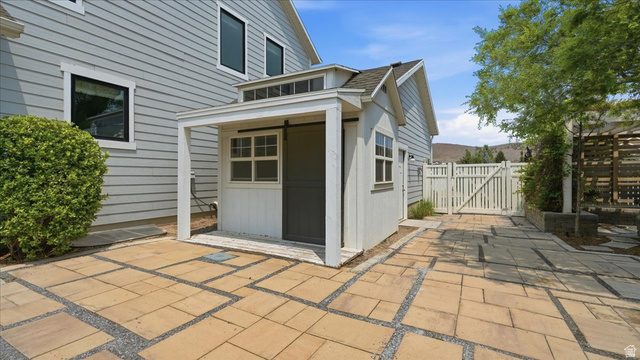 2038 East Ranch Road Eagle Mountain, UT 84005 - Photo 44 of 66 Patio area featuring square pavers and gravel accents, a detached shed with a sliding barn door, a white picket fence, and mature landscaping