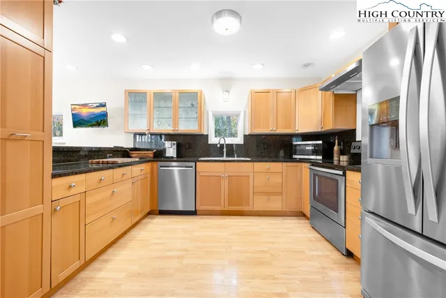 a kitchen with stainless steel appliances granite countertop a refrigerator a sink dishwasher a stove and white countertops with wooden floor