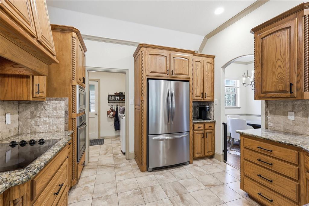 149 Overton Ridge Circle Weatherford, TX 76088 - Photo 14 of 39 Gourmet kitchen featuring wood cabinetry, stainless steel appliances, stone countertops, and a tiled backsplash