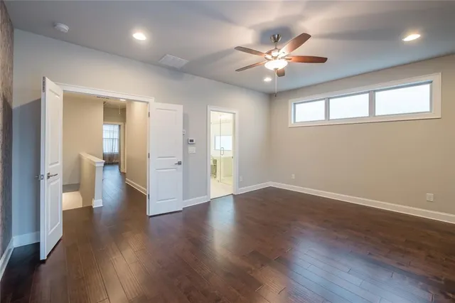 a view of an empty room with wooden floor and a ceiling fan