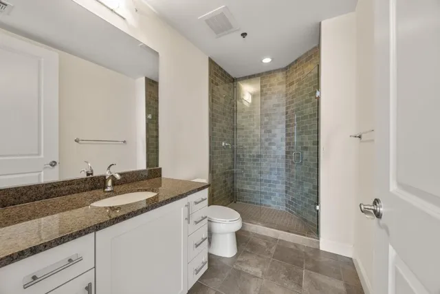 a bathroom with a granite countertop sink a toilet a mirror and shower