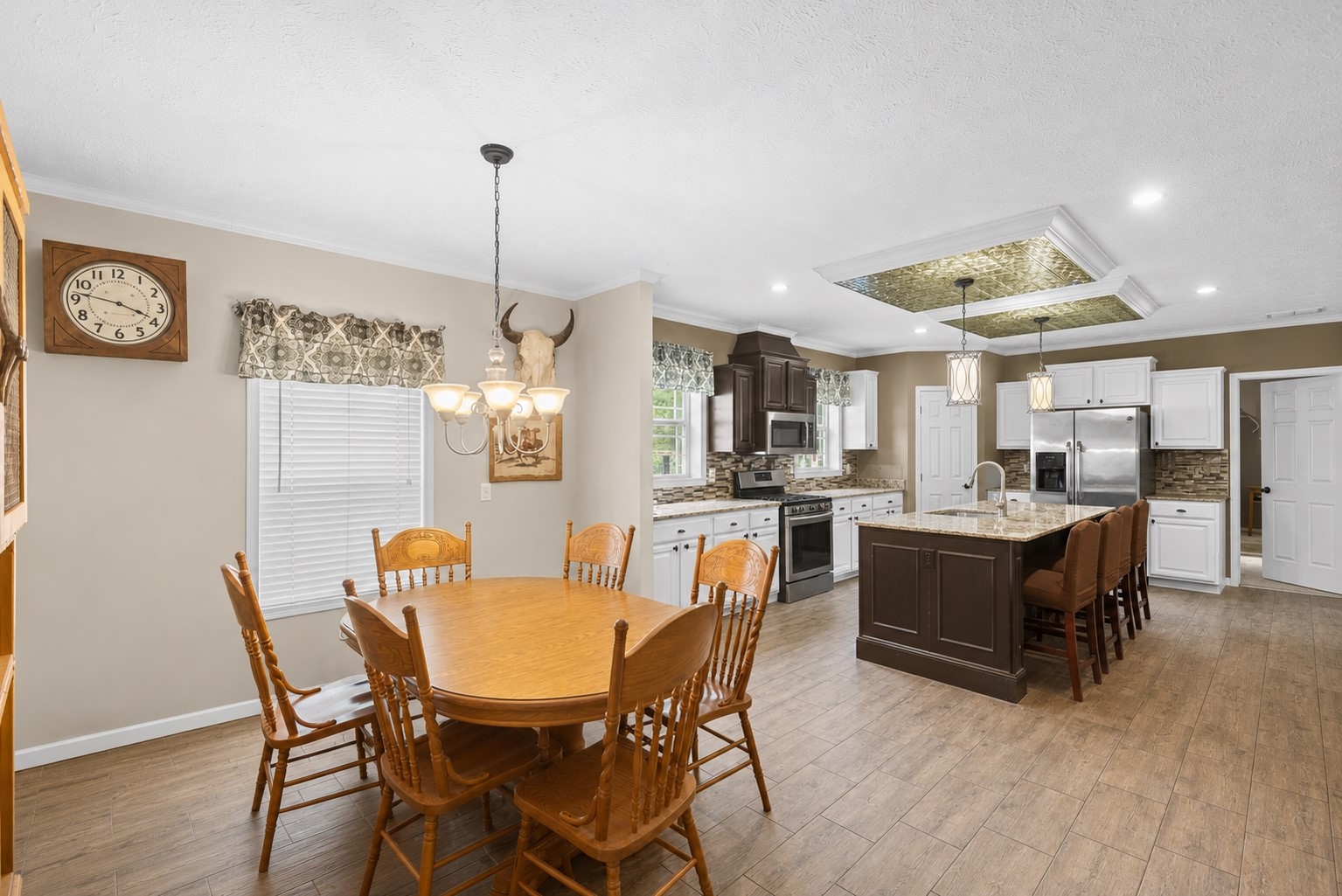 1800 2110th Road Hugo, OK 74743 - Photo 10 of 27 Open-concept kitchen and dining area featuring wood-finish flooring, two-tone cabinetry with stainless steel appliances, a center island with countertop seating, and a decorative recessed ceiling