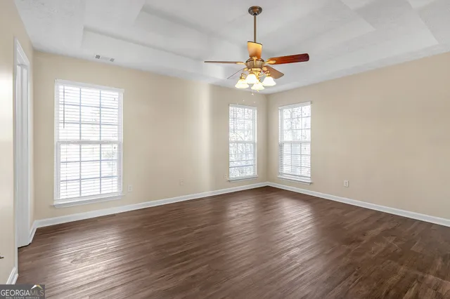 an empty room with wooden floor chandelier fan and windows