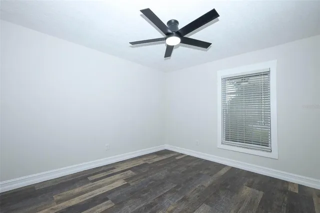 an empty room with wooden floor ceiling fan and window
