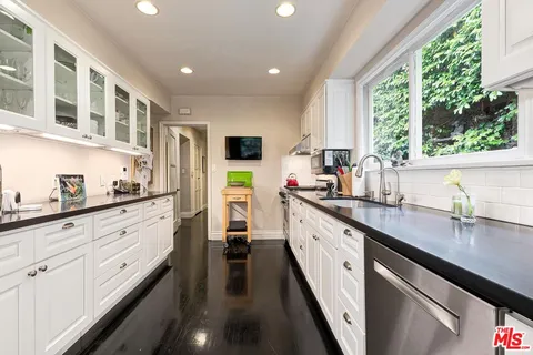 a kitchen with granite countertop lots of white cabinets and wooden floor