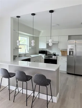 a kitchen with stainless steel appliances granite countertop a sink a refrigerator a stove a dining table and chairs with wooden floor