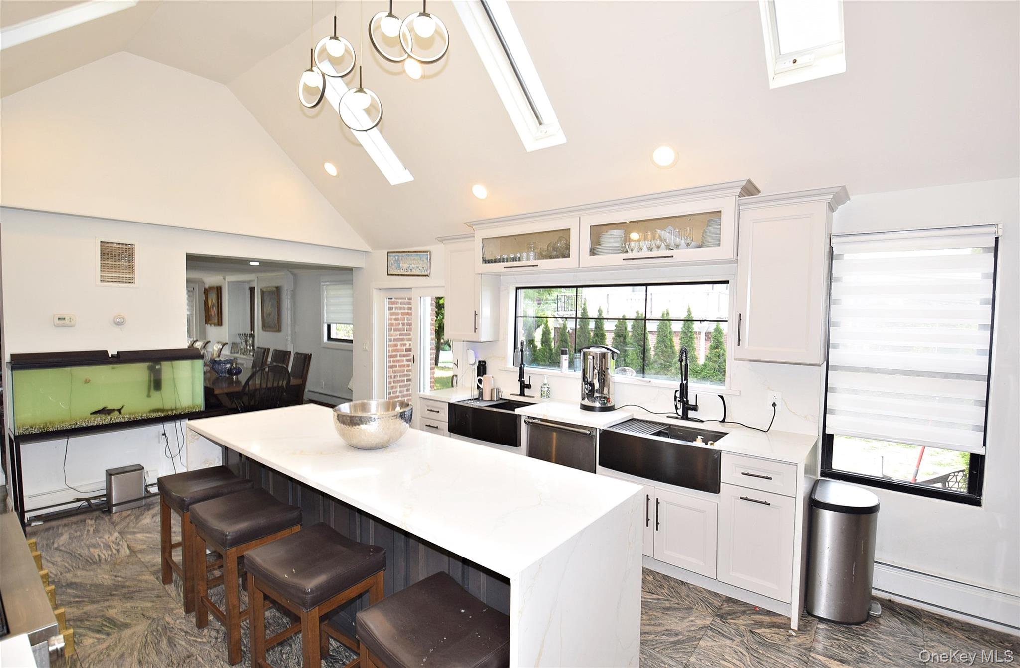 25 Old Mill Road Great Neck, NY 11023 - Photo 35 of 45 Vaulted ceiling with skylights, contemporary pendant lighting, white shaker cabinetry, dual stainless steel farmhouse sinks, and a large central island with seating