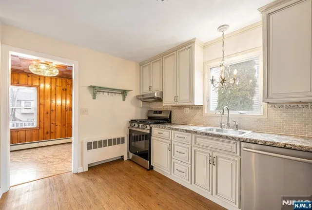 a kitchen with stainless steel appliances granite countertop a stove a sink and white cabinets with wooden floors