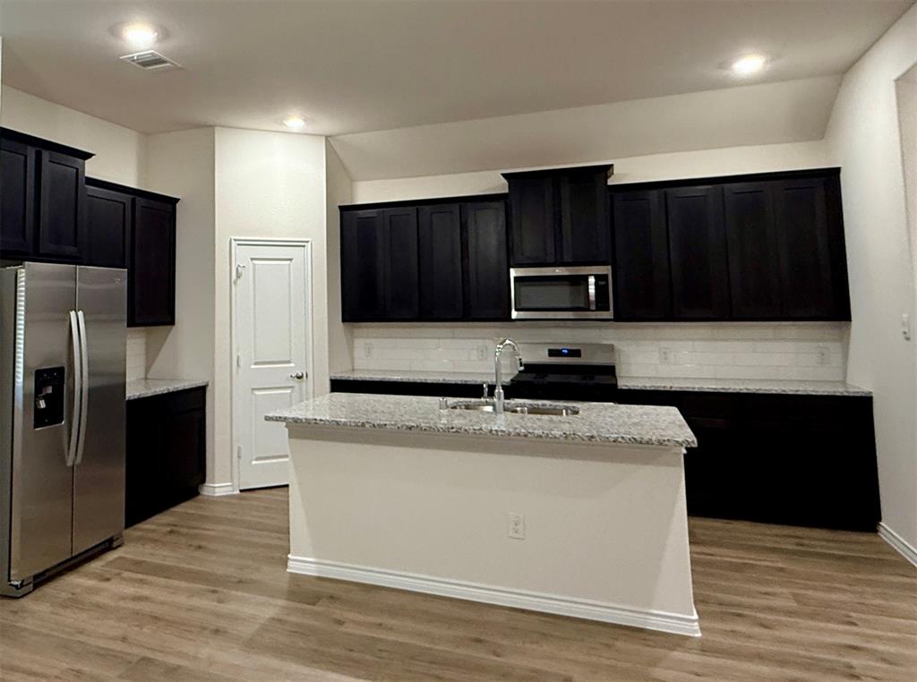 2025 Eugene Street Anna, TX 75409 - Photo 9 of 32 a kitchen with granite countertop wooden cabinets a refrigerator and a stove with wooden floor