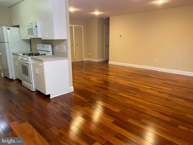 a view of kitchen and empty room with wooden floor