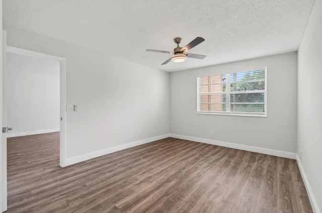 an empty room with wooden floor a ceiling fan and windows