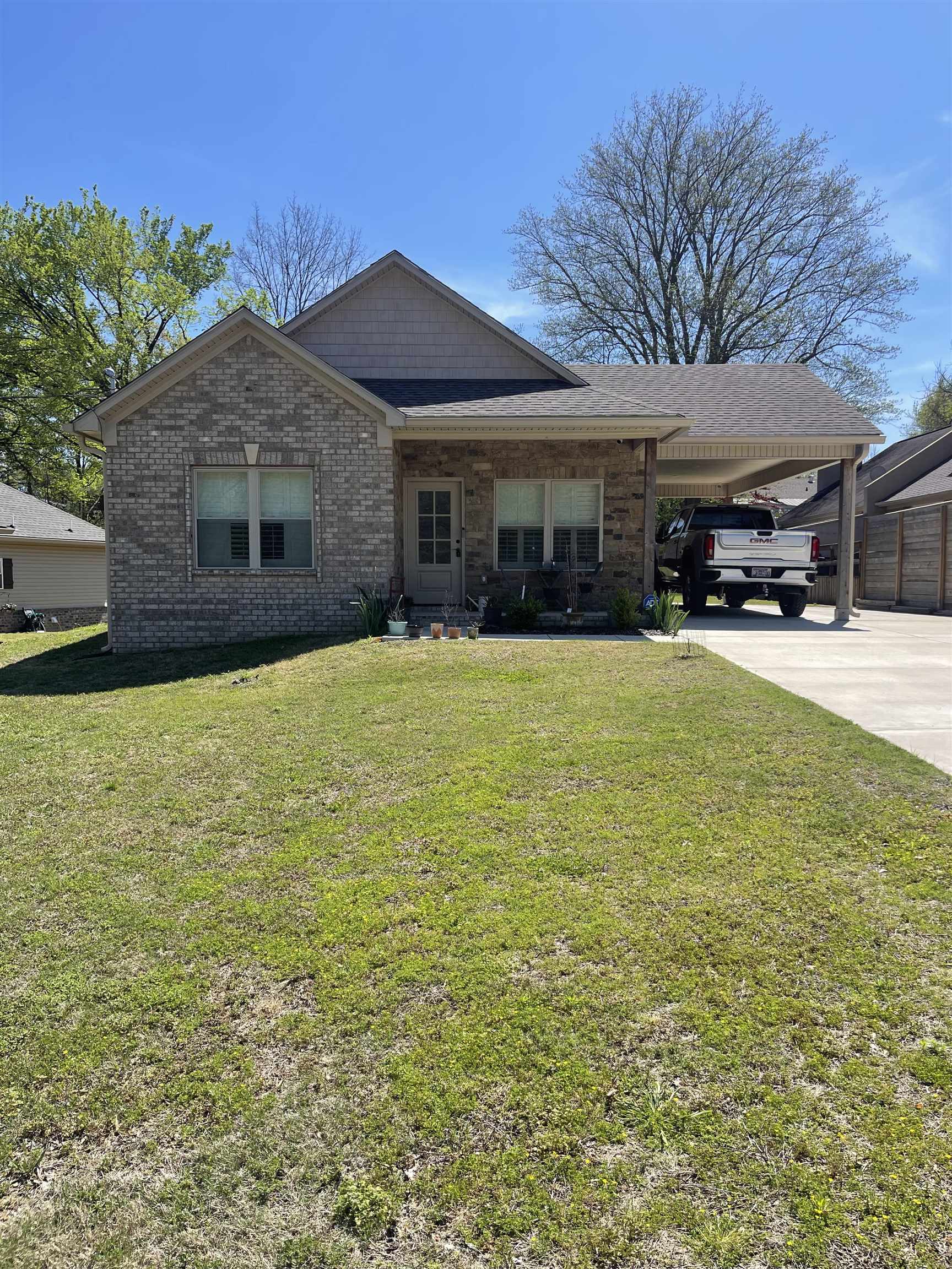 View of front of home with a carport, brick siding, a front lawn, and covered porch