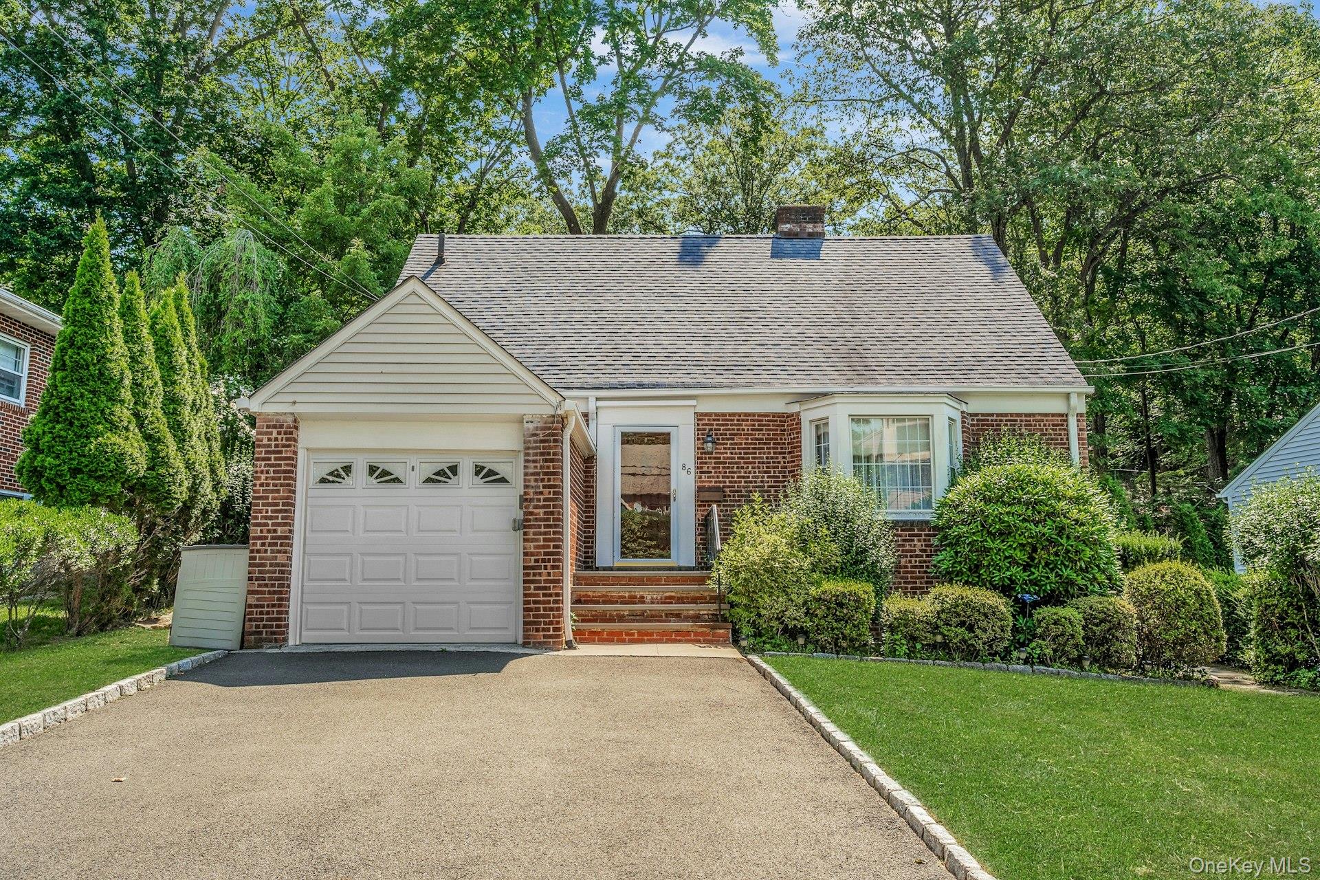 86 Briary Road Dobbs Ferry, NY 10522 - Photo 1 of 1 View of front facade featuring brick siding, an attached garage, asphalt driveway, and a shingled roof