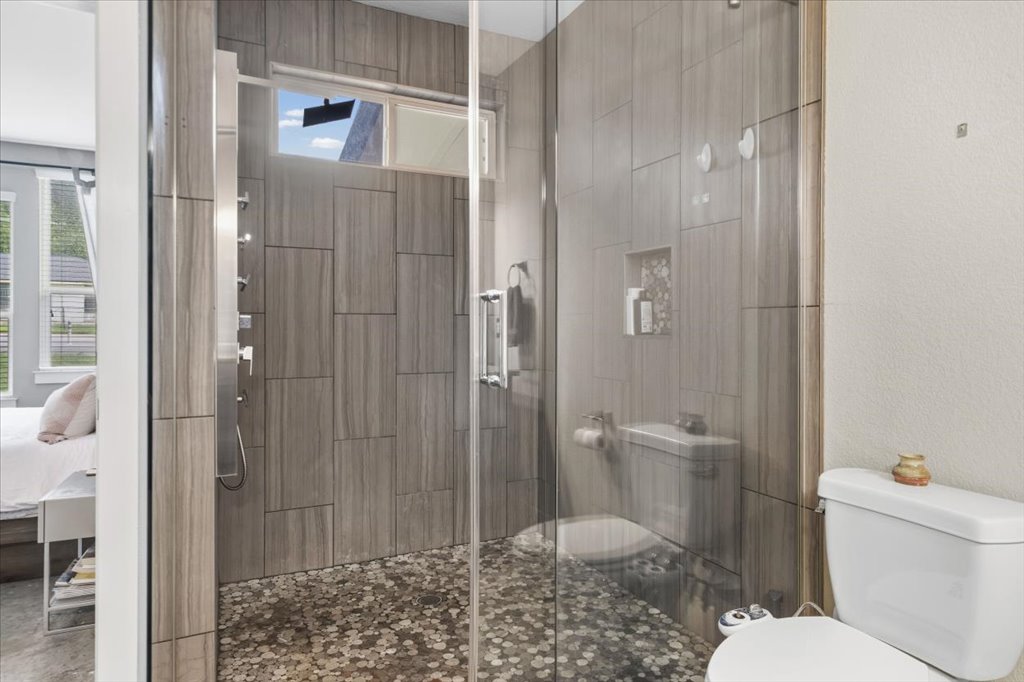 1800 Webberville Road, Unit B Austin, TX 78721 - Photo 17 of 30 Glass-enclosed shower featuring wood-grain tile walls, a pebble floor, multi-function shower panel, and an integrated shower niche